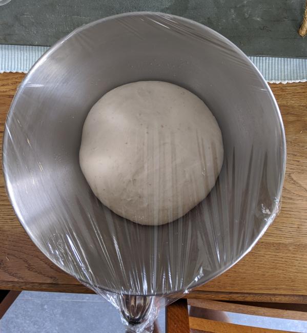 Pizza dough rising in covered silver bowl.